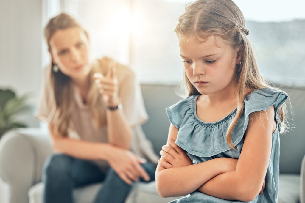Closeup of an adorable little girl standing with arms crossed and looking upset while being scolded