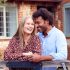 Portrait Of Loving Couple By Gate Holding House Keys Outside New Home In Countryside